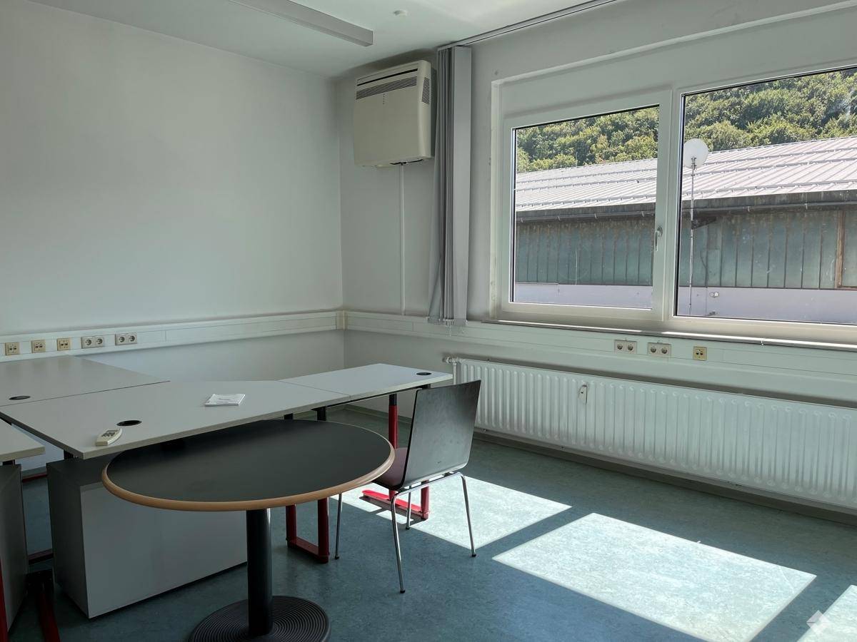 Funktionales Büro mit hellgrünem Boden, großen Fenstern und Blick auf bewaldete Hügel.