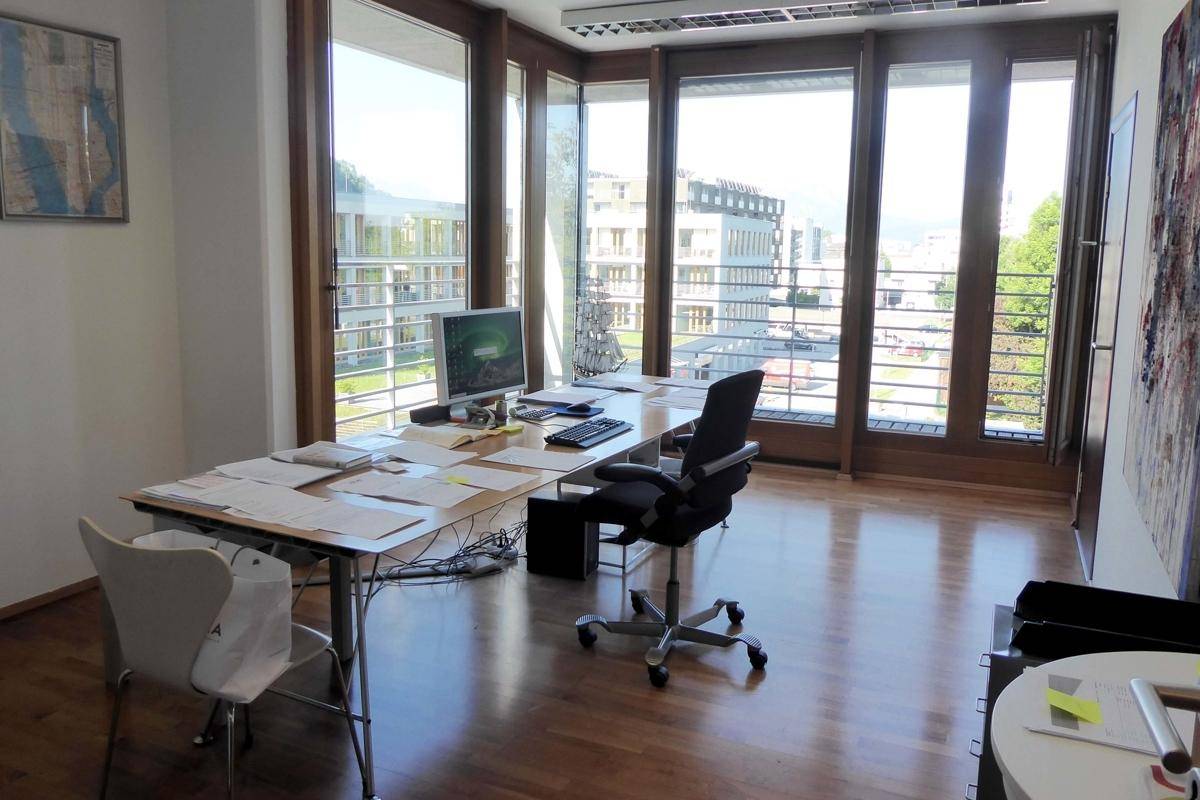 Geräumiges Büro mit Holzboden und einer Fensterfront, die viel Tageslicht hereinlässt.