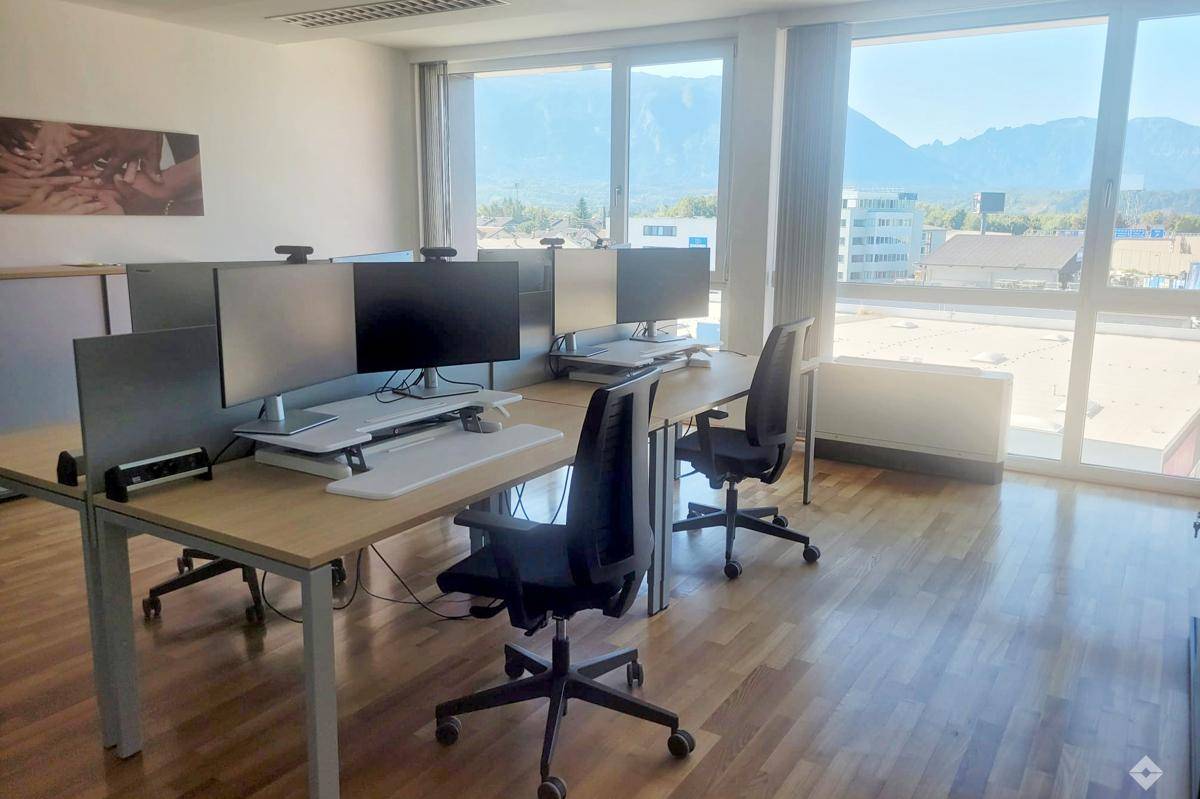 Moderner Büroraum mit mehreren Arbeitsplätzen, großen Fenstern und beeindruckendem Bergblick.
