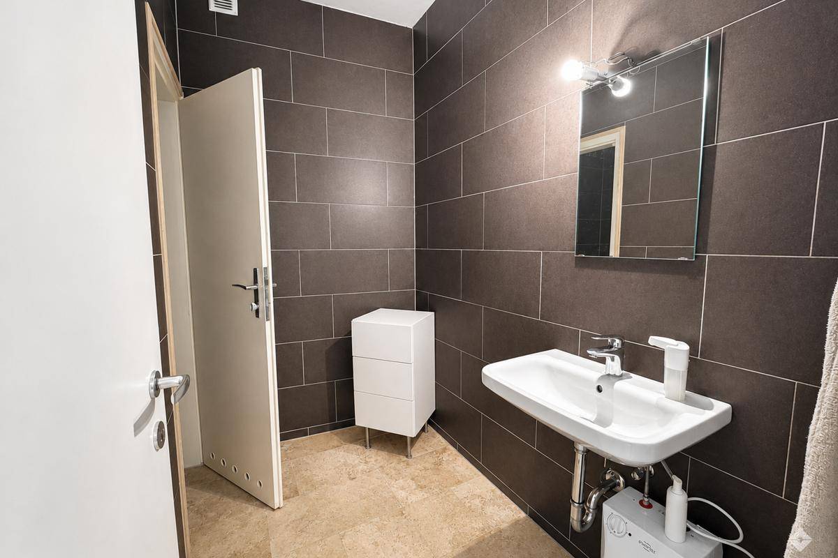Modernes Badezimmer mit dunklen Fliesen, Waschbecken und Spiegel.