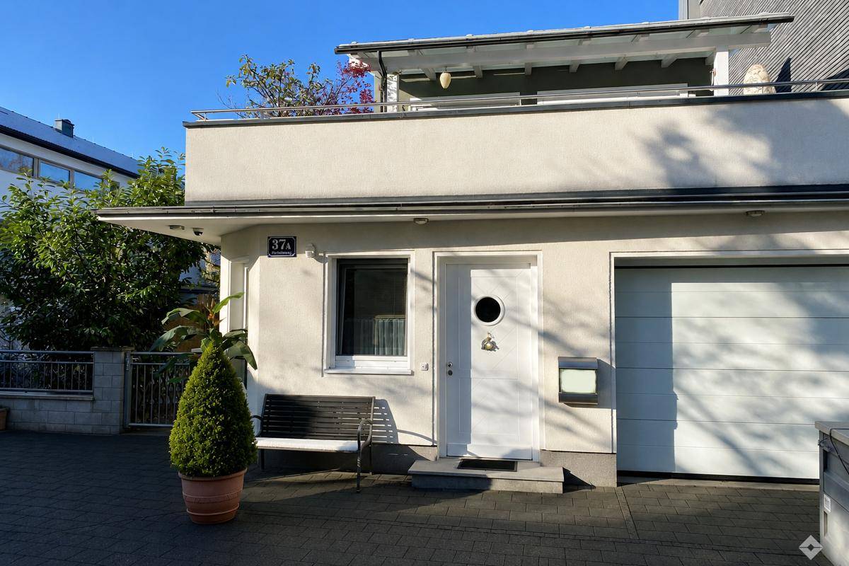 Eingangsbereich eines modernen Gebäudes mit Garage und kleinem Balkon im Obergeschoss.