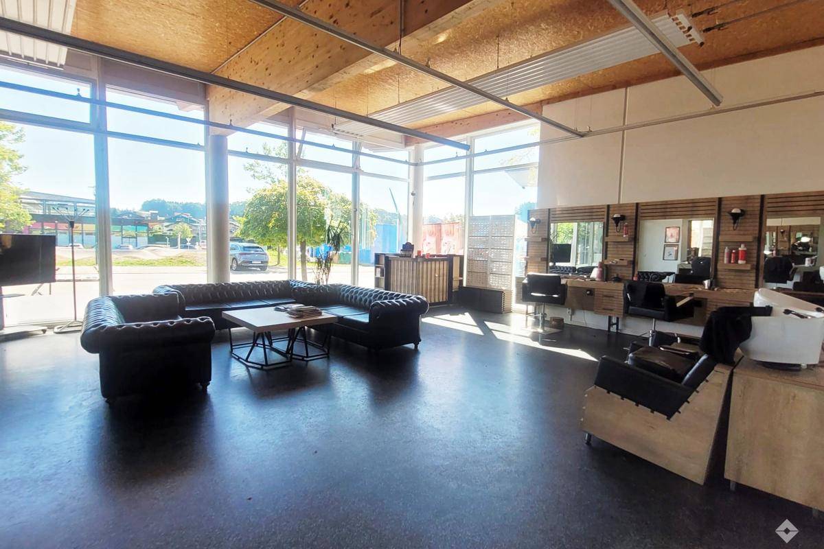 Weitläufiger Gewerberaum mit viel Tageslicht, ausgestattet als Friseursalon, mit dunklem Boden und Holzdecken.