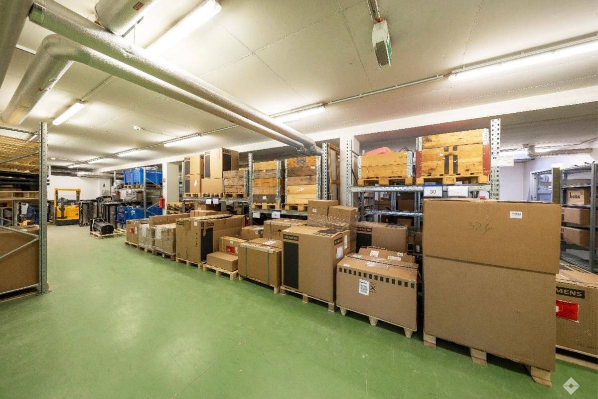 Geräumiger Werkstattbereich mit Arbeitsplatte, Regalen und Blick auf den Außenparkplatz durch das Rolltor.