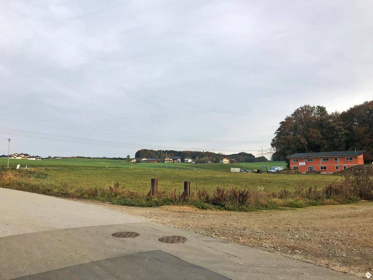 Grüne Wiesen und ein Gebäude mit roter Fassade unter bewölktem Himmel, umgeben von Bäumen.