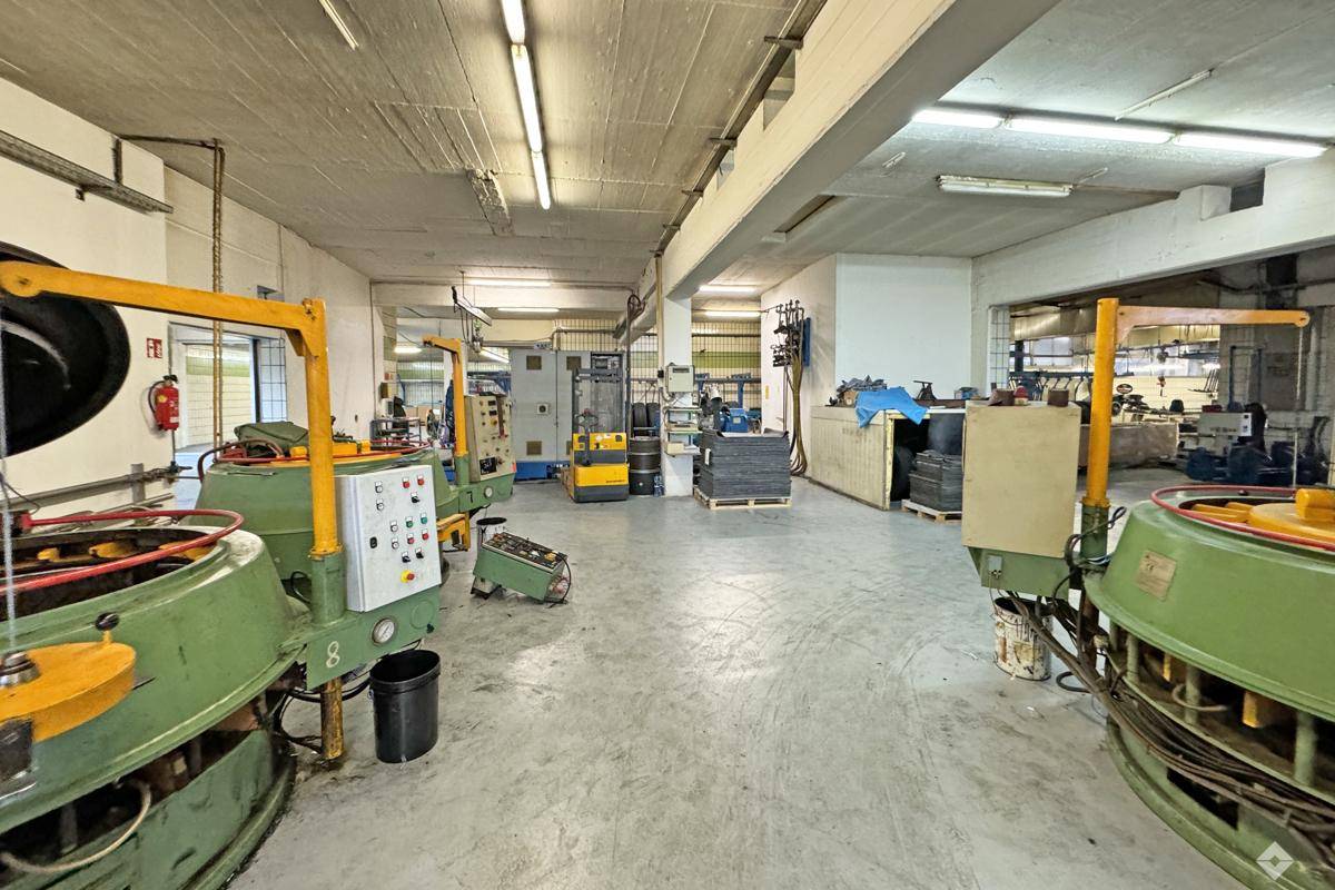 Industrielle Produktionshalle mit verschiedenen Maschinen, Betonboden und Deckenbeleuchtung.