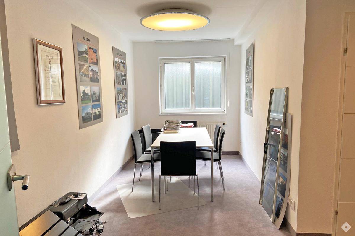 Kleiner Besprechungsraum oder Büro mit einem Tisch, schwarzen Stühlen und einem Fenster an der Stirnseite.