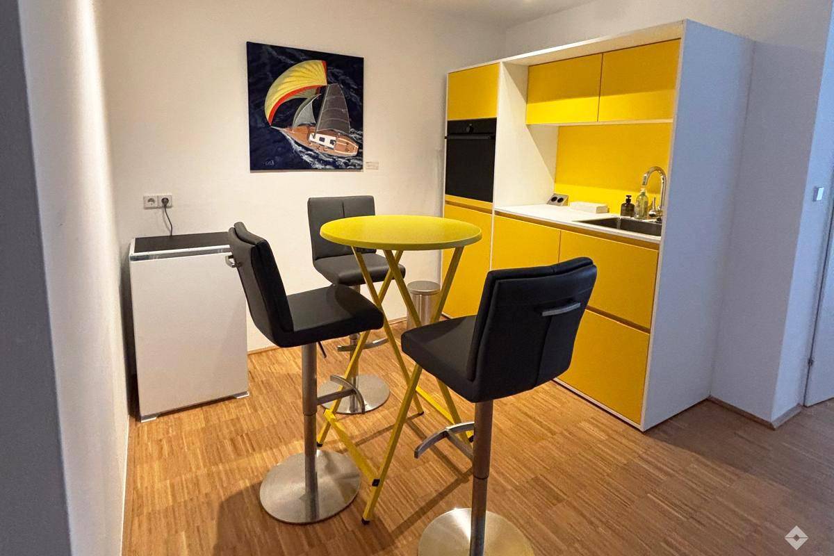Moderne Küchenzeile in leuchtendem Gelb mit integriertem Backofen, Kühlschrank und einem passenden Bartisch.