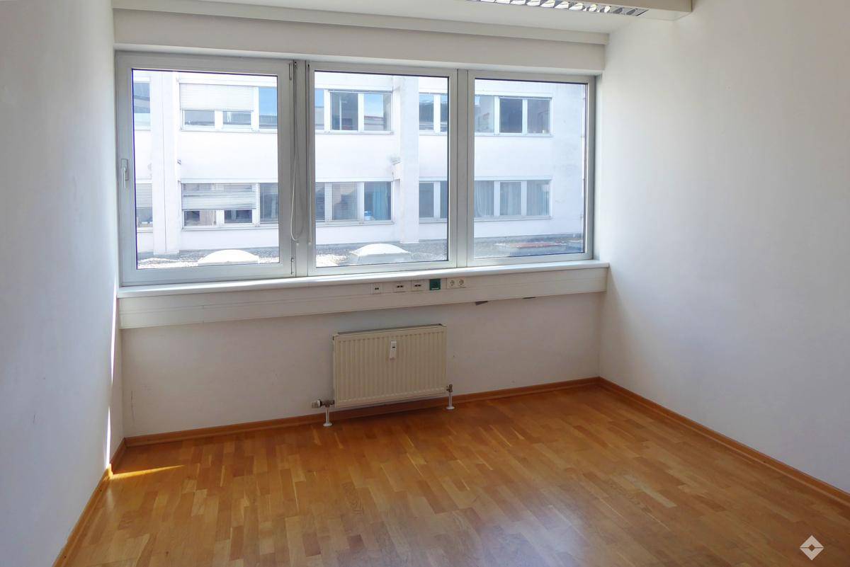 Heller Büroraum mit großen Fenstern, Holzfußboden und Heizkörper unter der Fensterbank.
