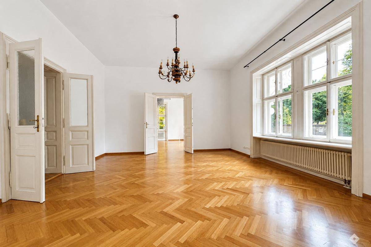 Heller Wohnraum mit Fischgrätparkett, hohen Fenstern und einem klassischen Kronleuchter, der viel Tageslicht hereinlässt.