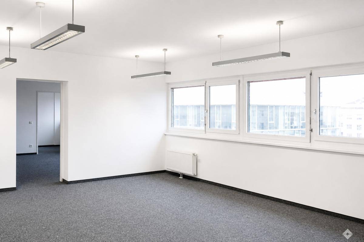 Leeres Büro mit moderner Beleuchtung, großen Fenstern und einem sauberen grauen Teppichboden.