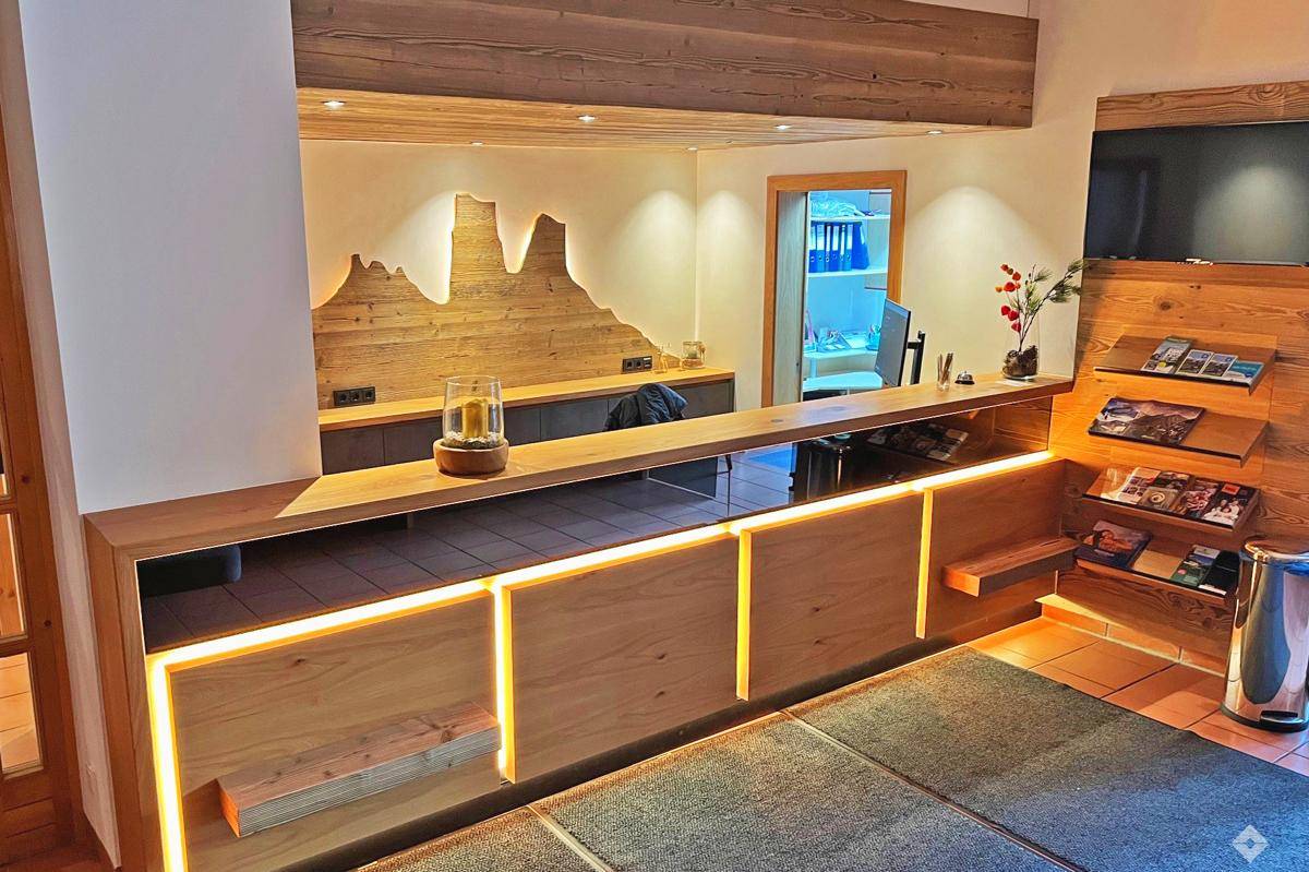 Empfangsbereich mit beleuchteter Holztheke und dekorativer Wandgestaltung im Hintergrund.