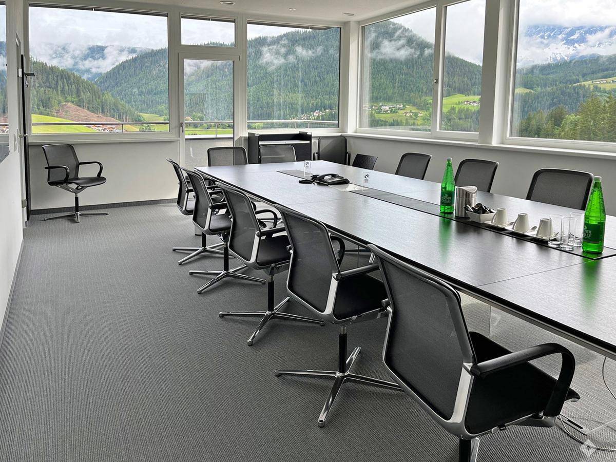 Geräumiger Konferenzraum mit großem Tisch, bequemen Stühlen und beeindruckendem Bergblick durch Panoramafenster.