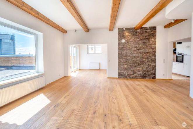 Geräumiges Wohnzimmer mit Holzbalken, Holzboden und einer Akzentwand aus Ziegeln.