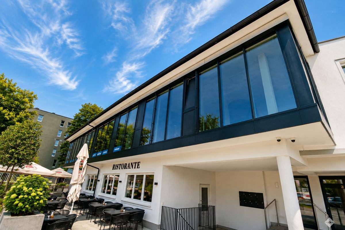 Nahaufnahme der modernen Glasfassade des Gebäudes mit einem Restaurantbereich und Außensitzplätzen im Erdgeschoss.