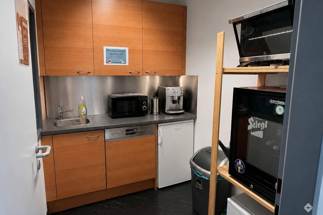 Funktionale Teeküche mit Holzschränken, Spülmaschine, Mikrowelle und Kaffeemaschine für Mitarbeiter.