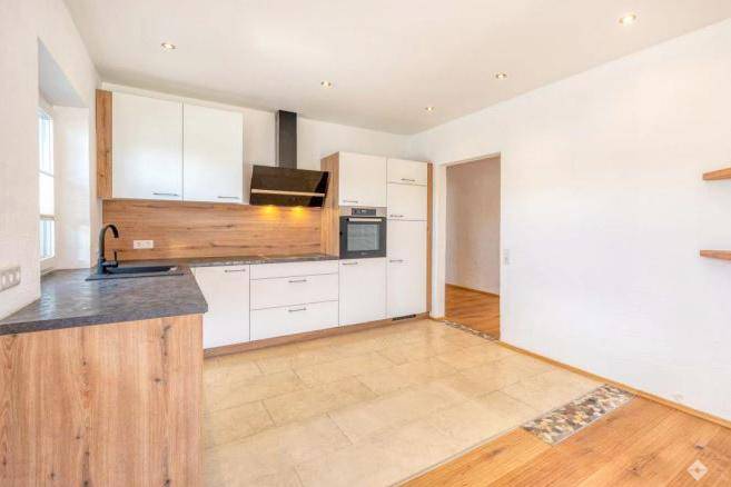 Moderne Küche mit weißen Schränken, Holzdetails und integrierten Geräten.