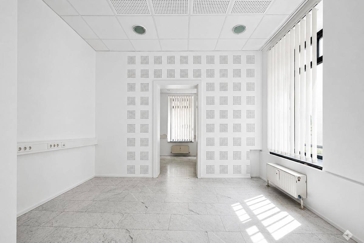 Großer, leerer Raum mit dunklem Teppichboden und langen Leuchtstoffröhren an der Decke.