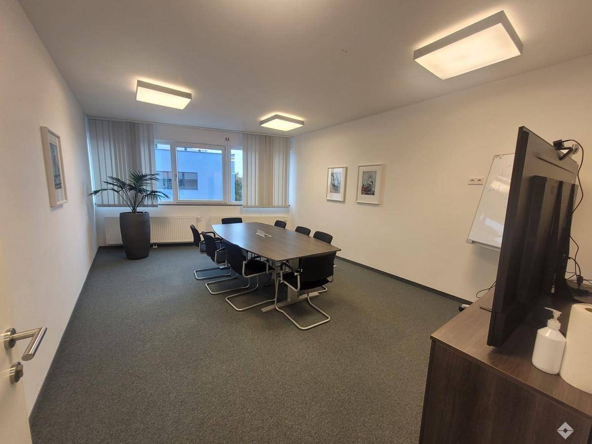 Geräumiger Konferenzraum mit großem Besprechungstisch, Teppichboden und viel Tageslicht von den Fenstern.
