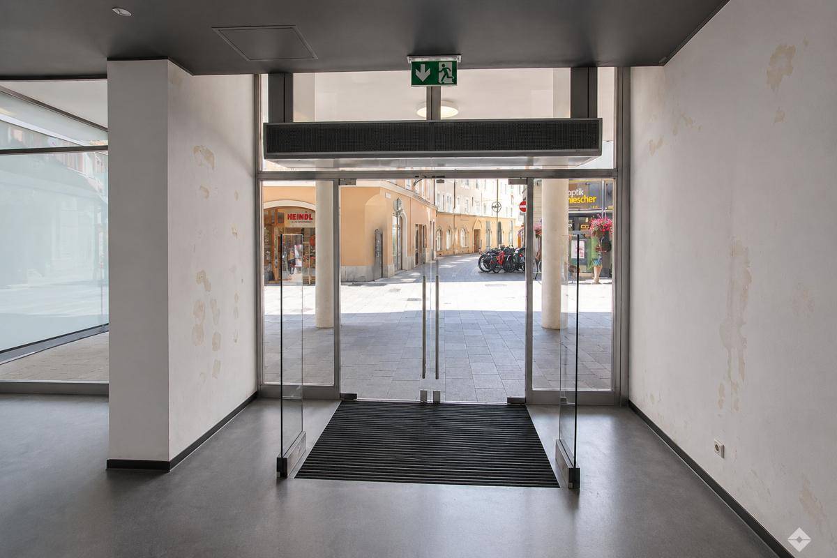 Eingangsbereich eines Geschäftsraums mit großen Glastüren und Blick auf die belebte Straße.