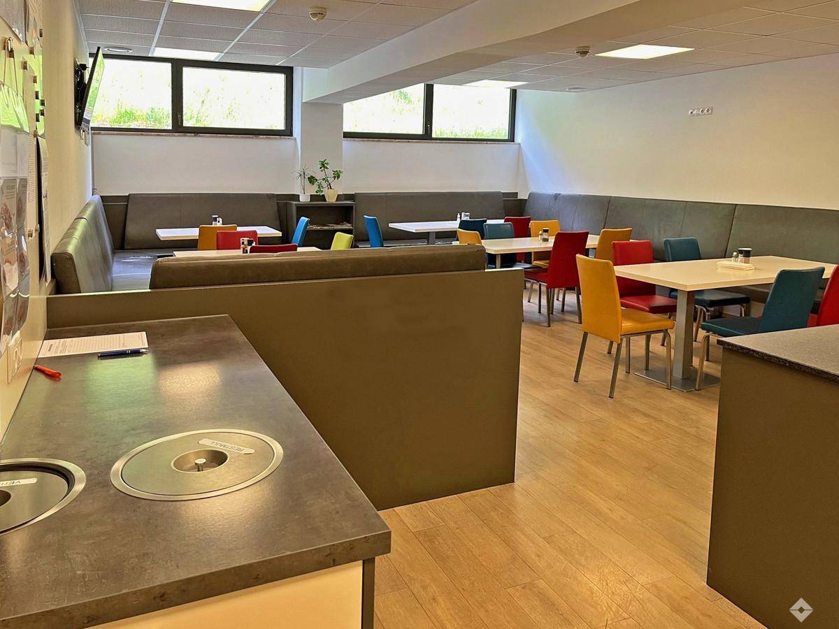 Moderne Cafeteria mit farbenfrohen Stühlen, bequemen Sitzbänken und einem praktischen Thekenbereich.
