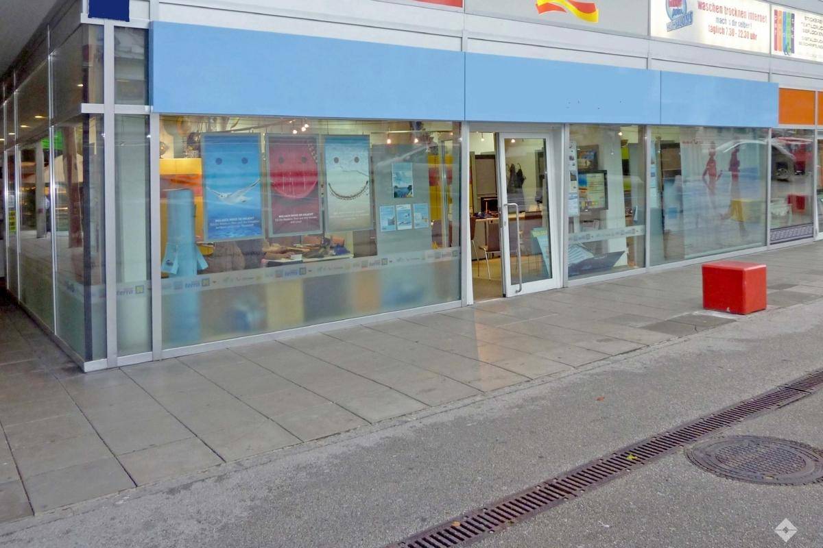 Innenansicht eines Büros oder Ladenlokals mit Arbeitsplätzen, Kundenbereich und großen Fenstern zur Straße.
