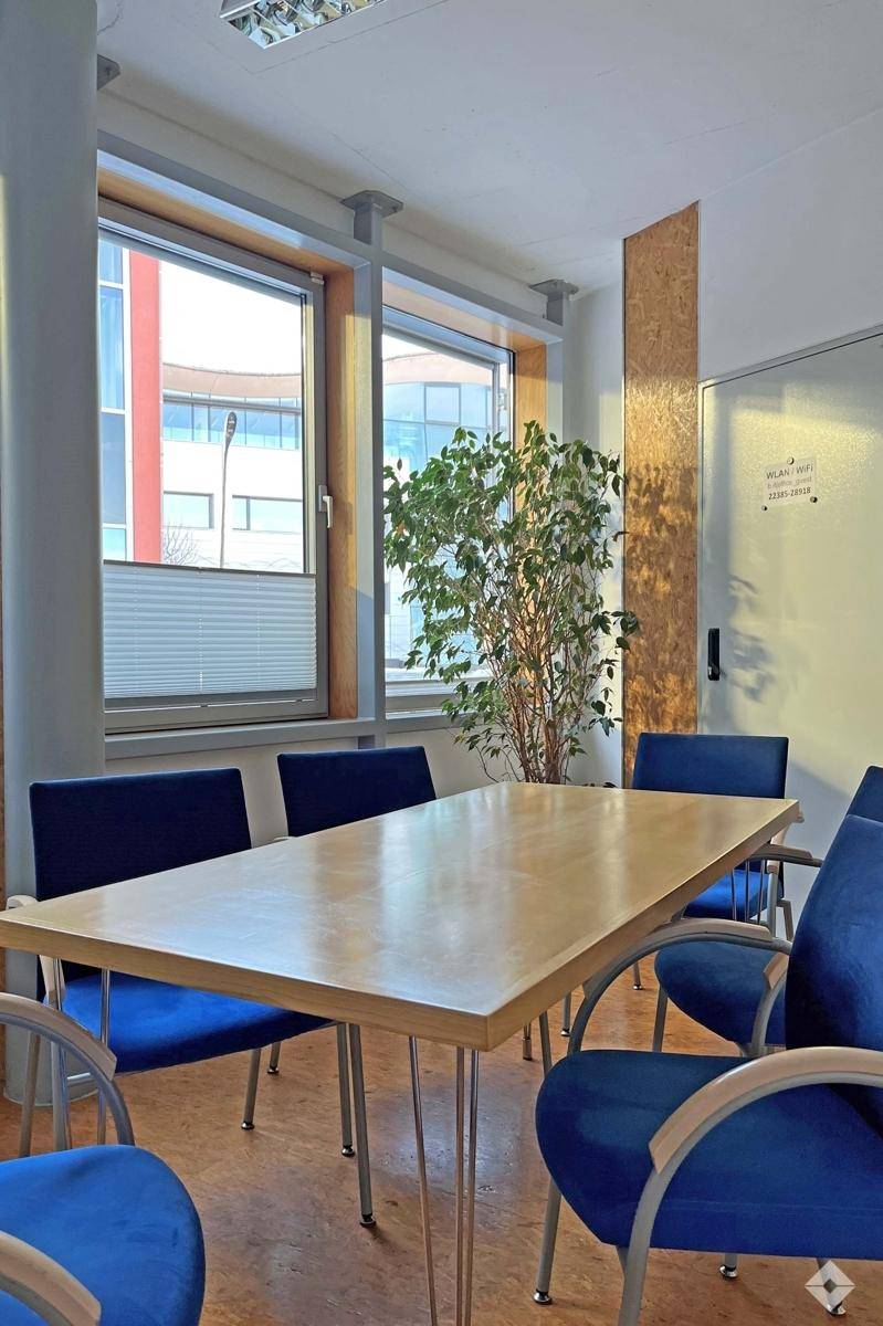 Konferenzraum mit großem Holztisch, blauen Stühlen und Fenstern mit Jalousien für Privatsphäre.