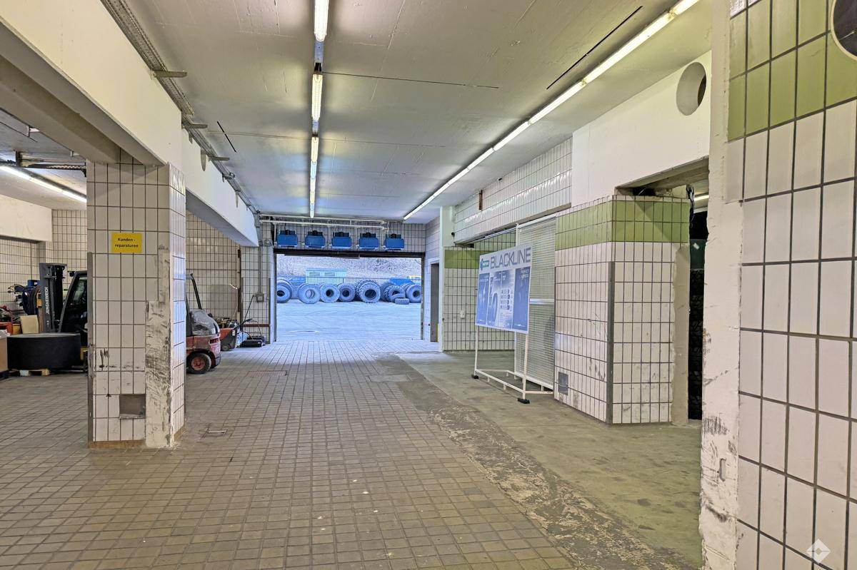 Geräumiger Lagerbereich mit gefliesten Wänden, Betonboden und Zugang zu einem Außenbereich mit Reifenstapeln.