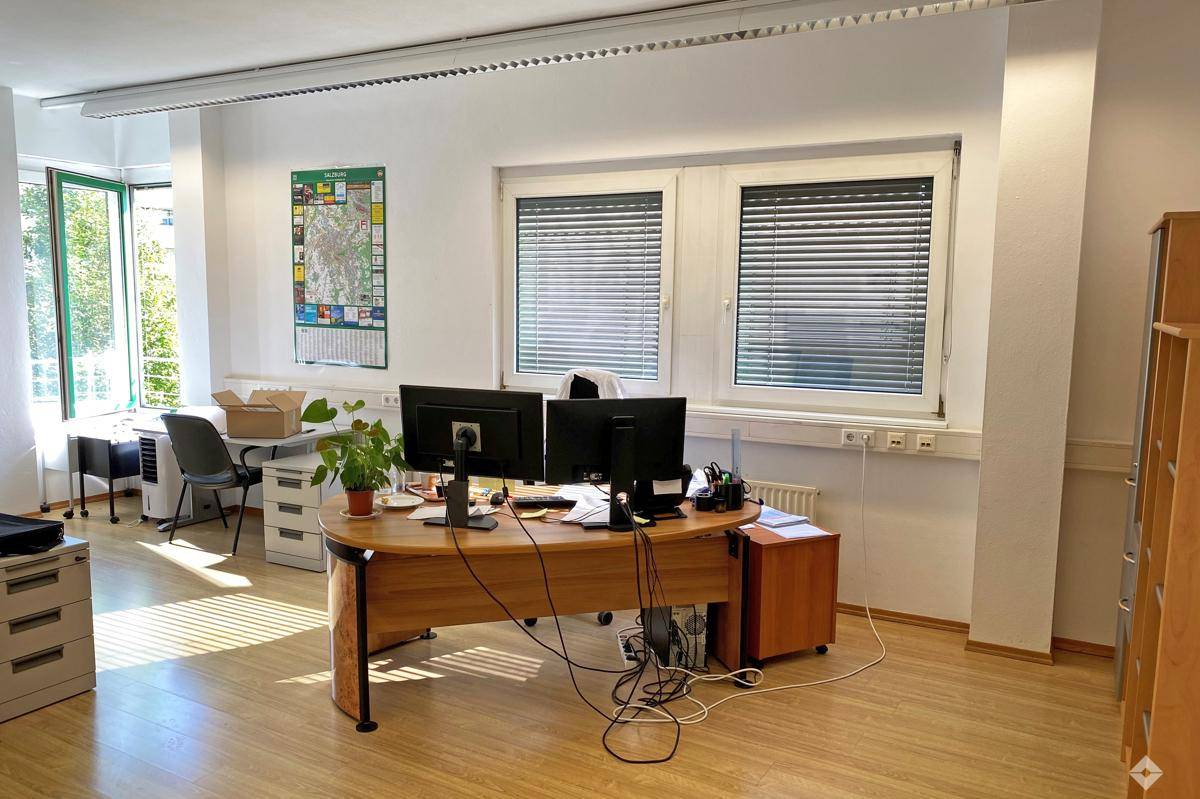 Geräumiges Büro mit mehreren Arbeitsplätzen, großen Fenstern und hellem Holzboden, ideal für ein Team.