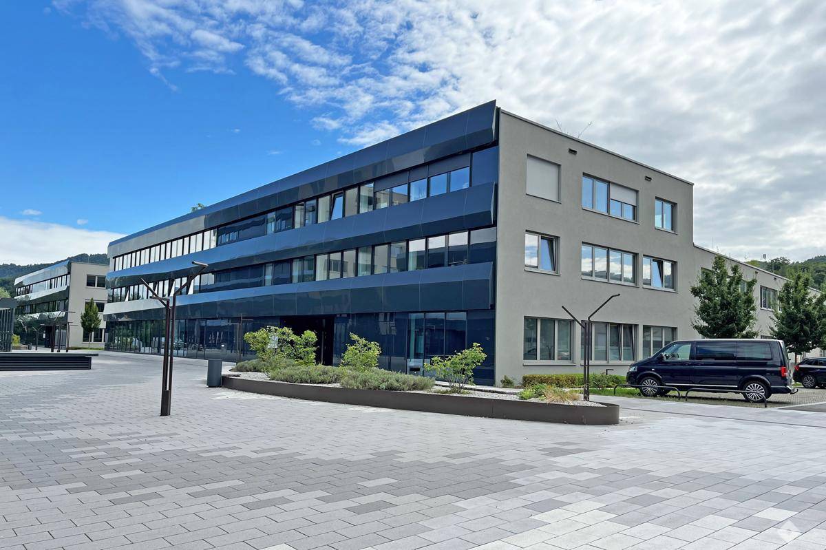 Moderne Bürogebäude mit dunkler Glasfassade und einem gepflegten Außenbereich mit Parkmöglichkeiten.