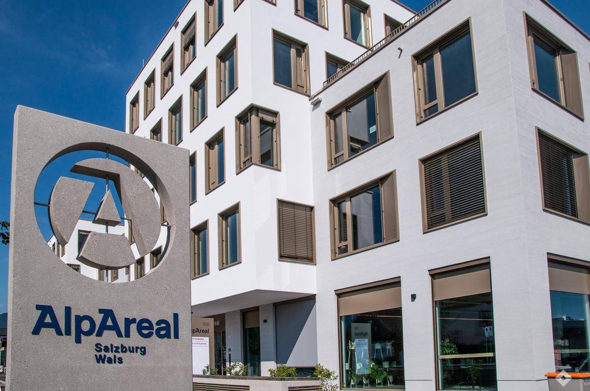 Modernes Gebäude mit weißer Fassade und zahlreichen Fenstern mit braunen Rahmen und Jalousien.