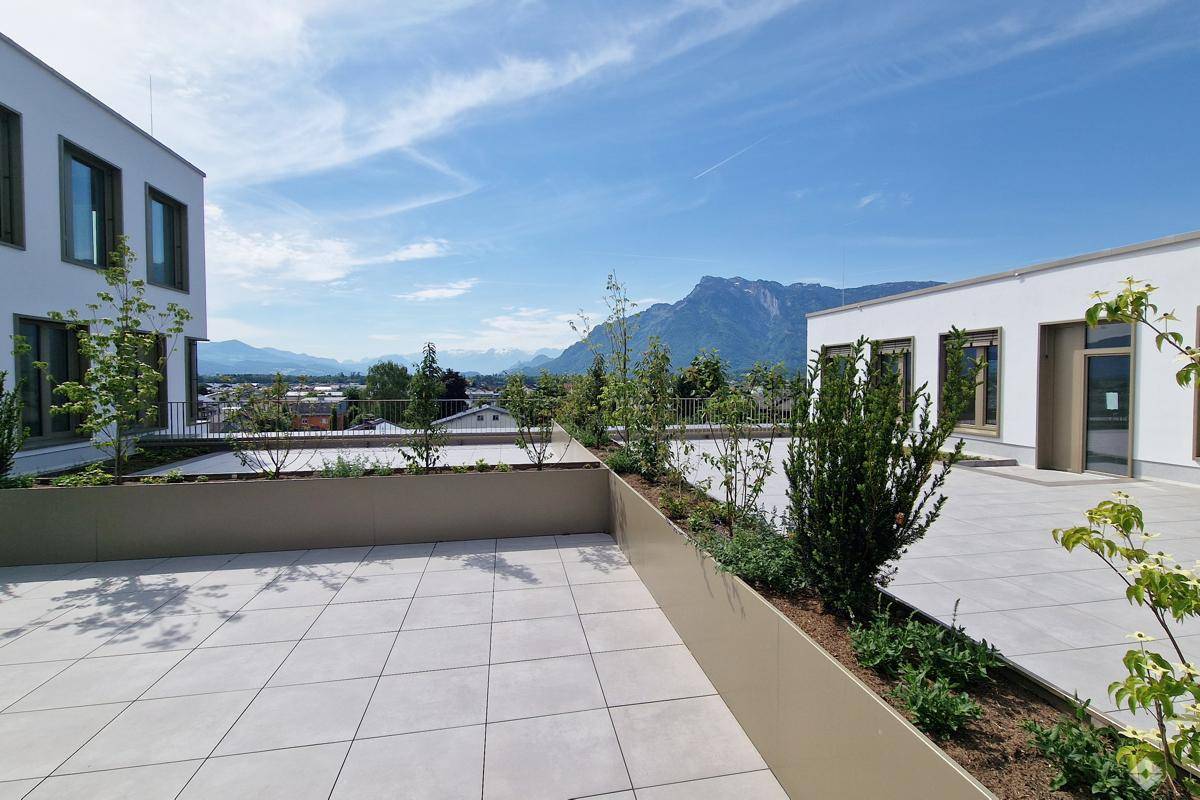 Große Dachterrasse mit modernen Fliesen, Pflanzenbeeten und einem weiten Blick auf die Berge und die Stadt.
