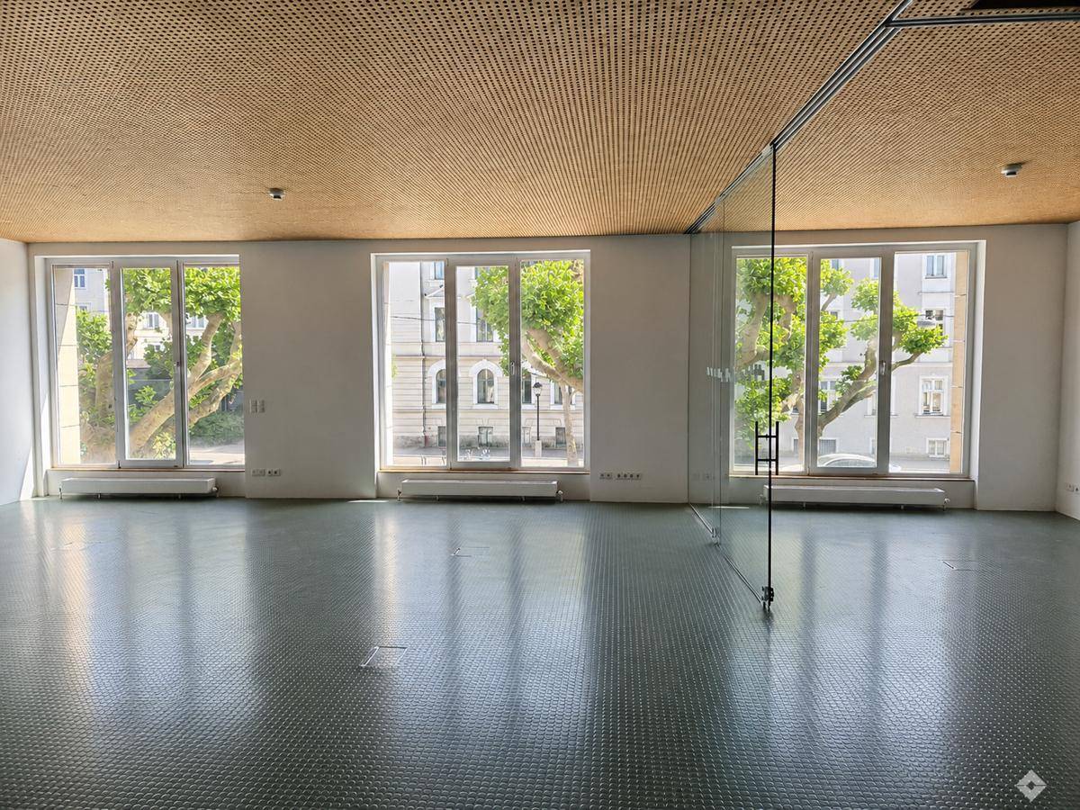 Leerer, heller Gewerberaum mit großen Fenstern, perforierter Holzdecke und Blick ins Grüne.