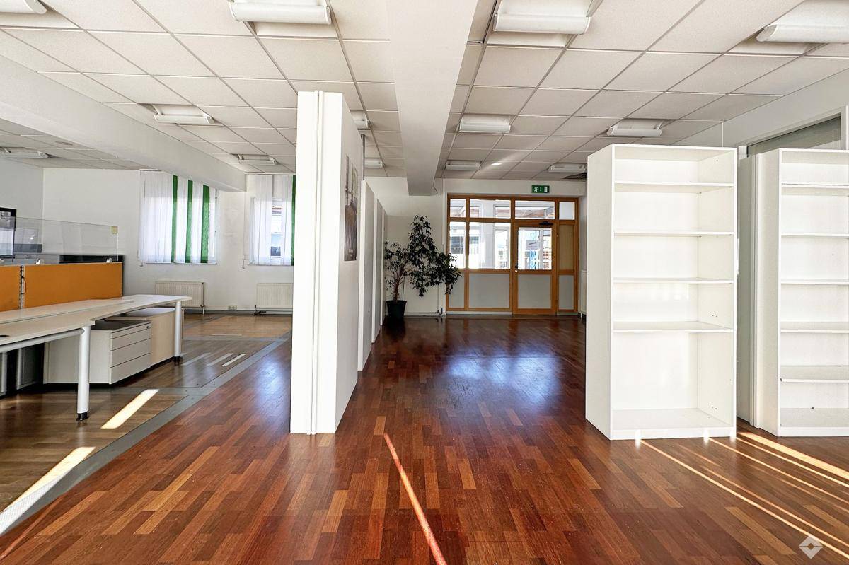 Geräumiges Büro mit Holzparkettboden, weißen Regalen und viel Tageslicht, ideal für offene Arbeitsbereiche.