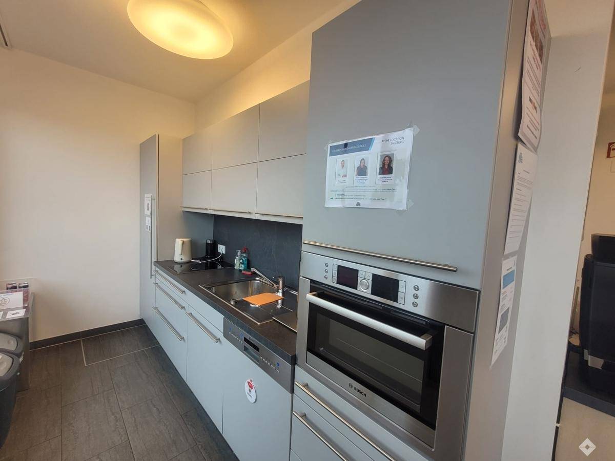 Moderne Küchenzeile mit grauen Schränken, integriertem Backofen und Geschirrspüler, ideal für eine Büroküche.