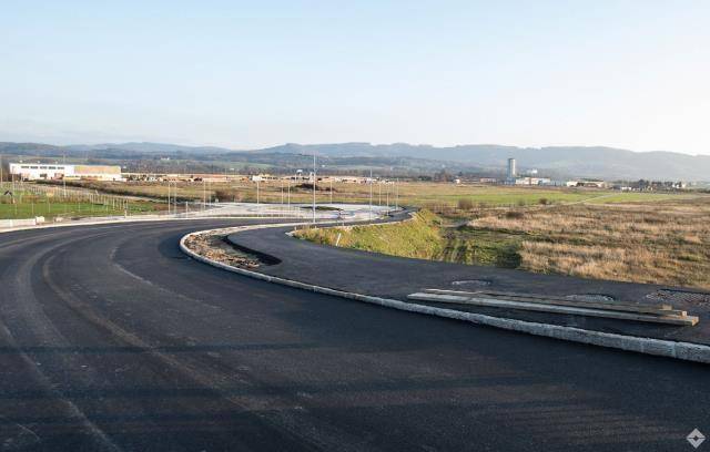 Blick auf eine neu angelegte Straße und Felder, umgeben von einer ländlichen Landschaft mit Hügeln im Hintergrund.