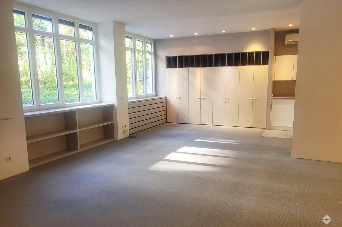Heller Büroraum mit großen Fenstern, die viel Tageslicht hereinlassen, und Einbauschränken.