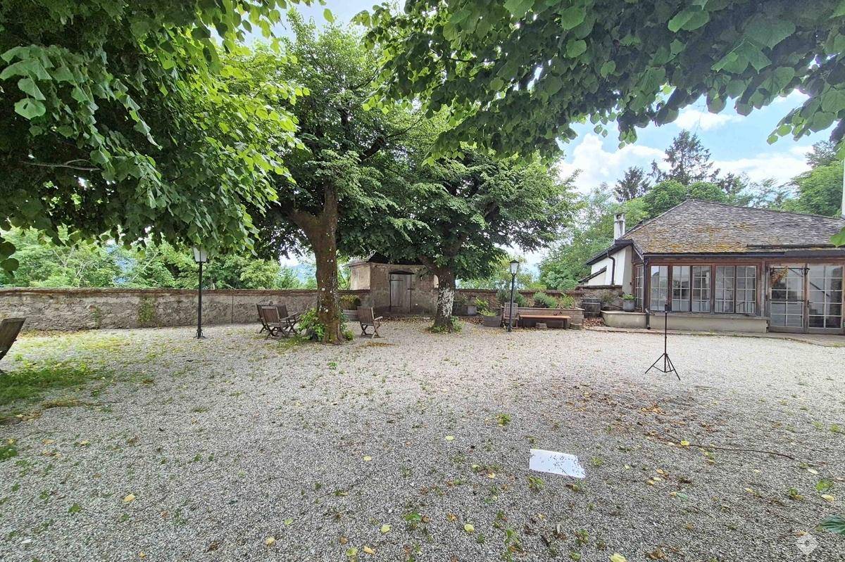 Weitläufiger Kiesgarten mit hohen Bäumen, Sitzgelegenheiten und Blick auf die Umgebung.