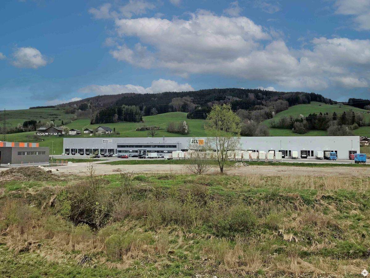 Modernes Industriegebäude mit Laderampen und weitläufiger Grünfläche, eingebettet in eine hügelige Landschaft.