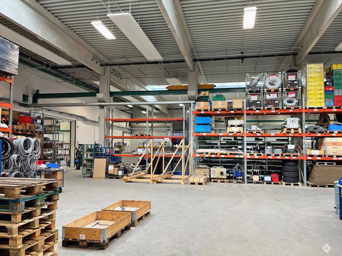 Geräumige Lagerhalle mit hohen Decken, industriellen Regalen und Paletten für effiziente Lagerung.