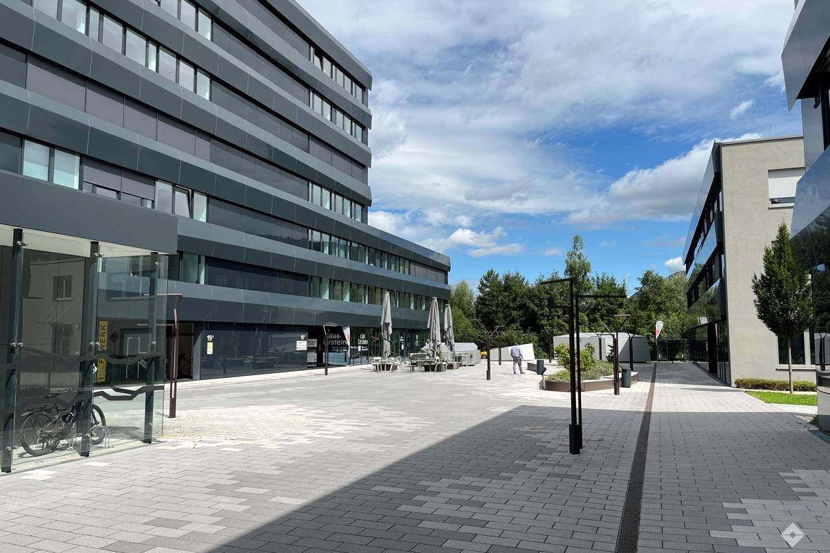 Moderne Bürogebäude mit dunklen Fassaden und einem weitläufigen, gepflasterten Vorplatz mit Sitzgelegenheiten.