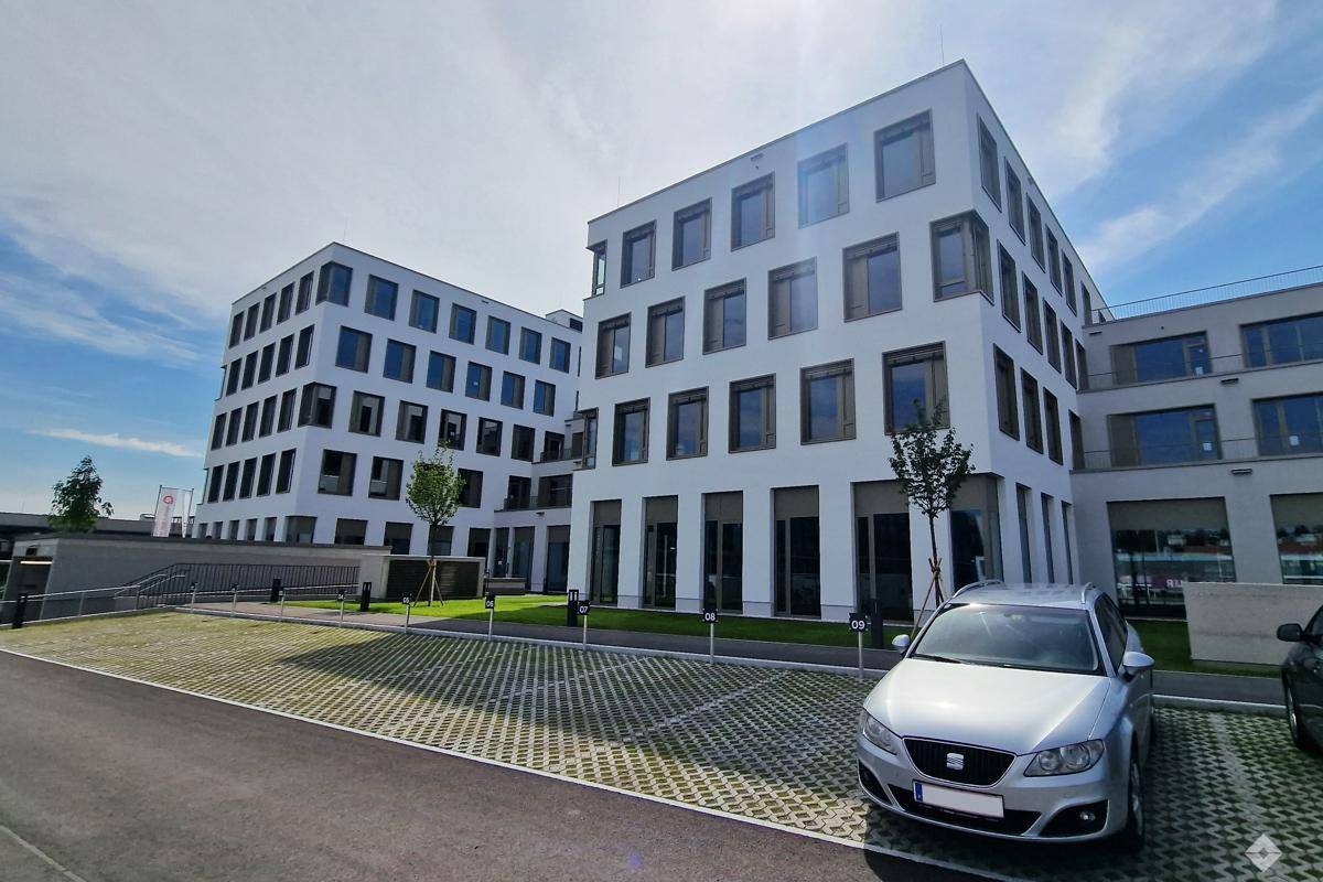 Außenansicht des modernen Bürokomplexes mit zwei Gebäudeteilen und einem großzügigen Parkplatzbereich im Vordergrund.