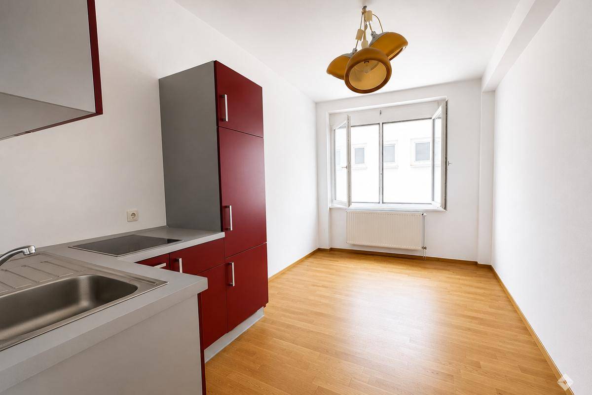 Kleine Küche mit roten Schränken, Spüle und Fenster, bereit zur Nutzung.