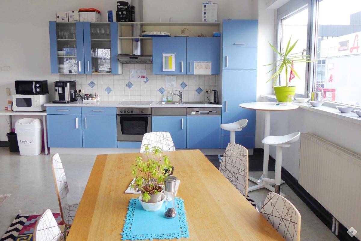Funktionale Küche mit blauen Schränken, einem Esstisch und einer kleinen Bar am Fenster.