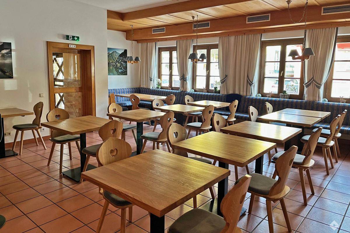Geräumiger Speisesaal mit vielen Holztischen und Stühlen, Terrakottafliesen und Fenstern.
