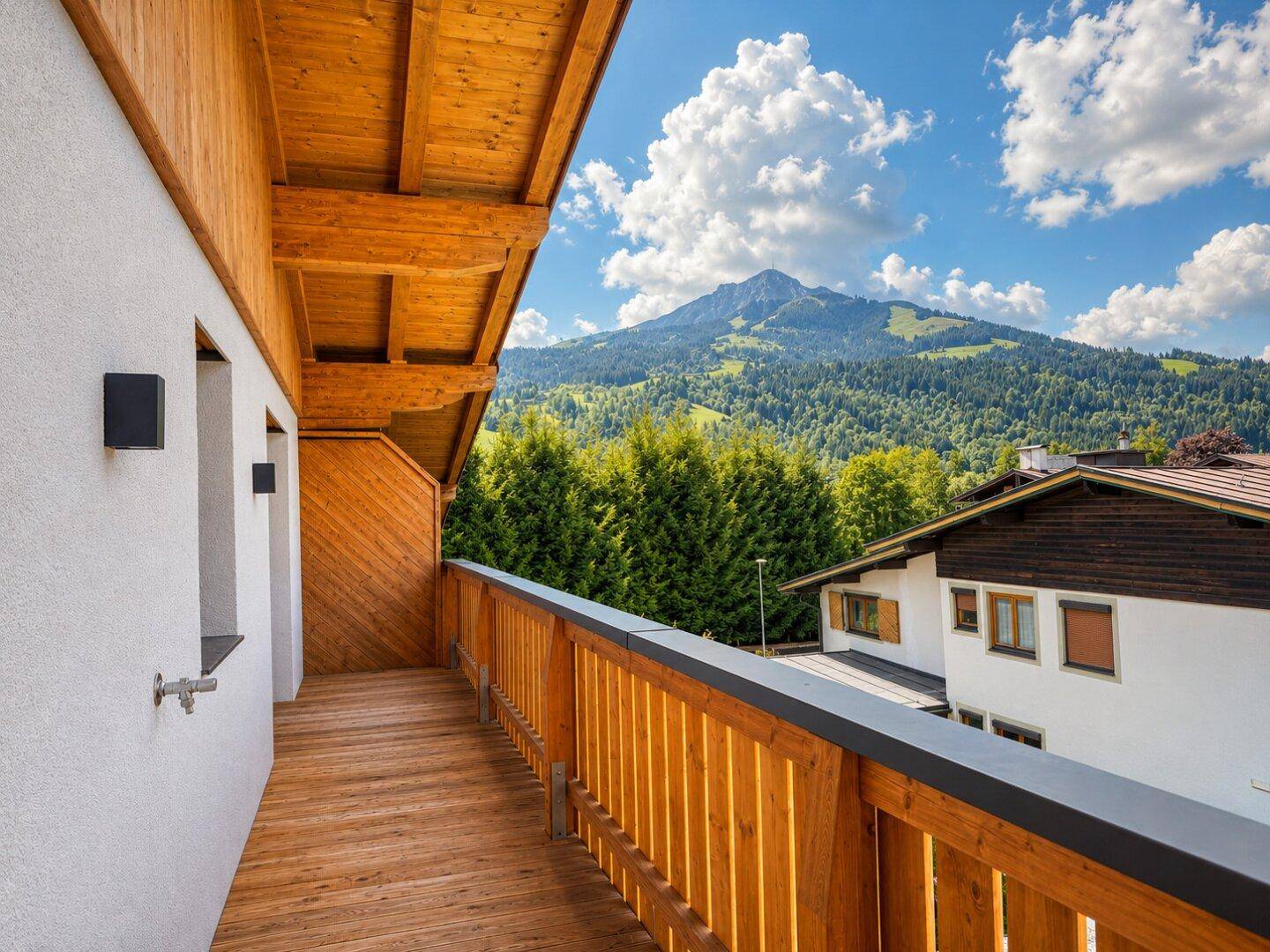 Holzbalkon mit Bergblick und grüner Umgebung unter blauem Himmel.