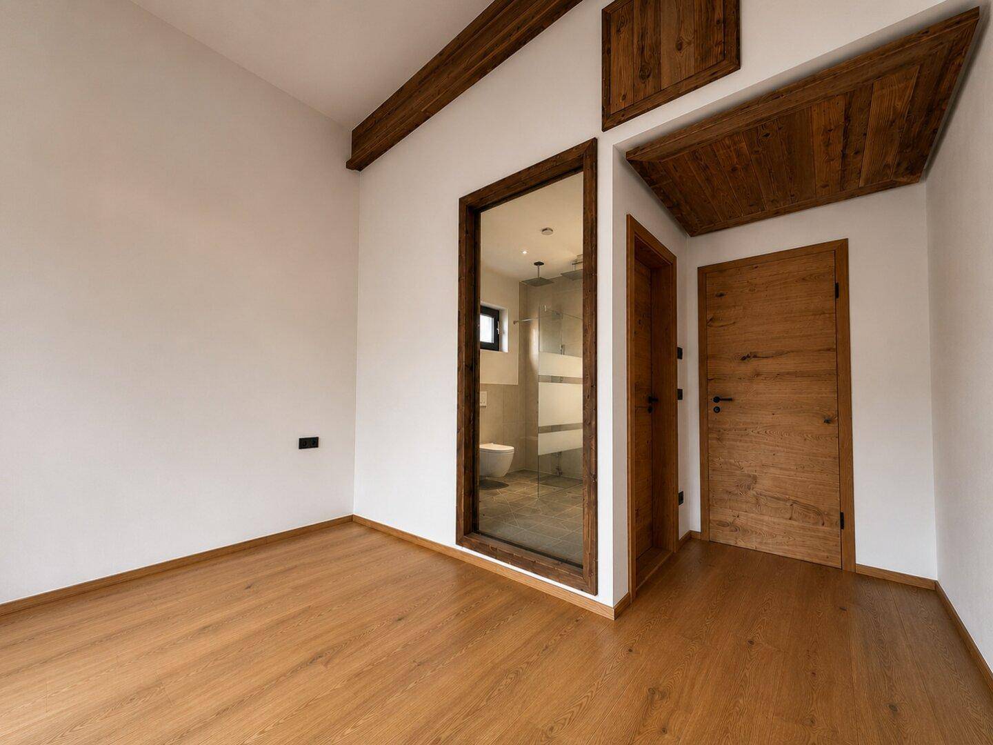 Leerer Raum mit Holzboden und integriertem Badezimmer mit Glaswand.