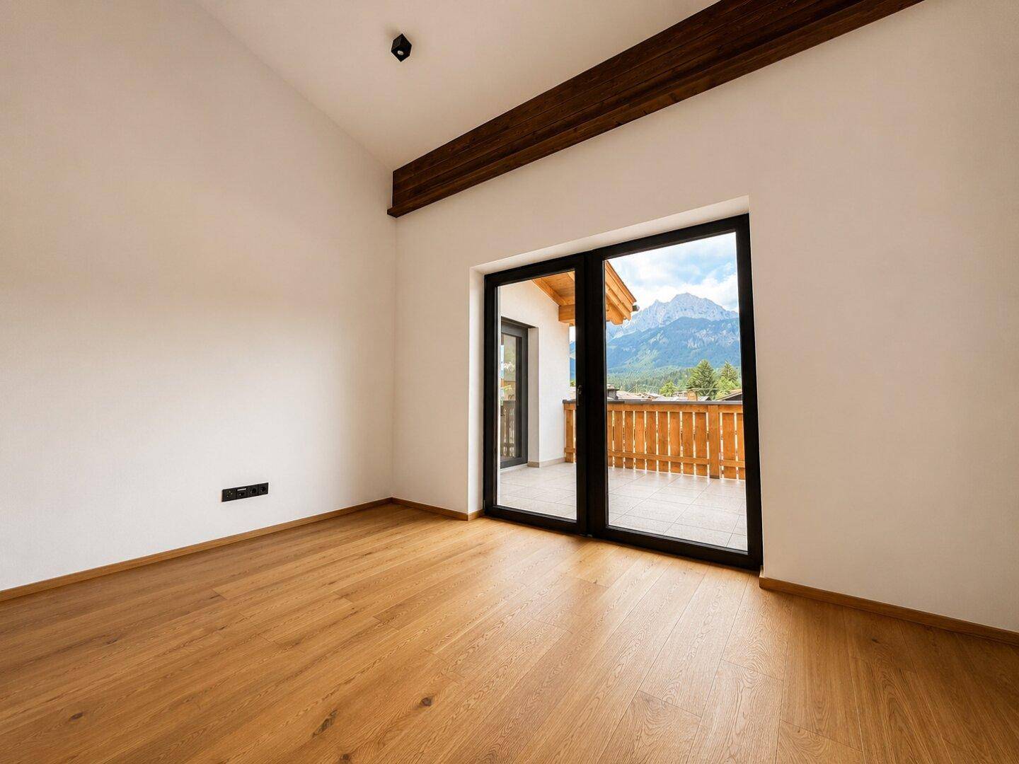 Leerer Raum mit Holzboden und Zugang zu einem Balkon mit Bergblick.