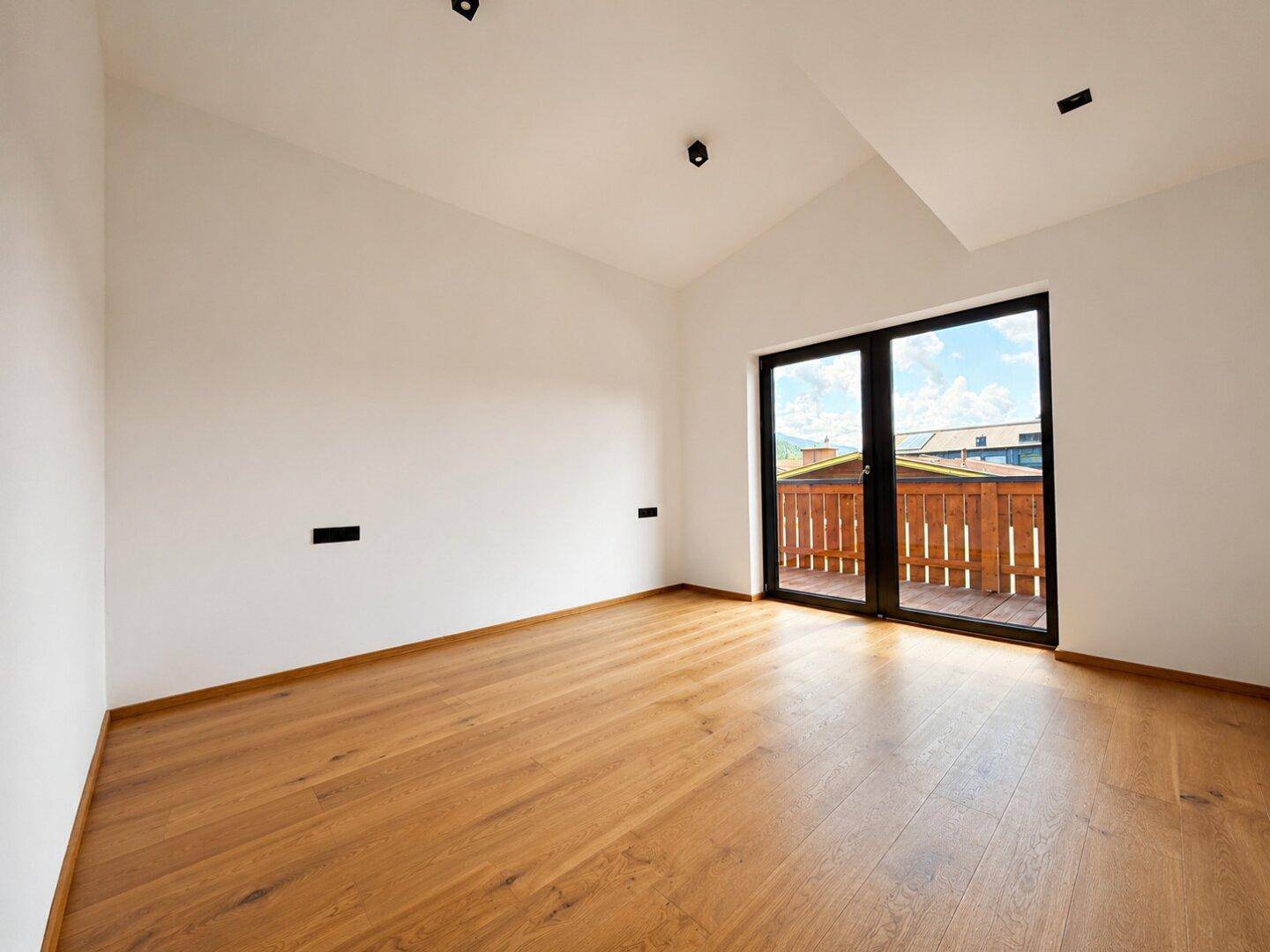 Leerer Raum mit Holzboden und Zugang zu einem Balkon.