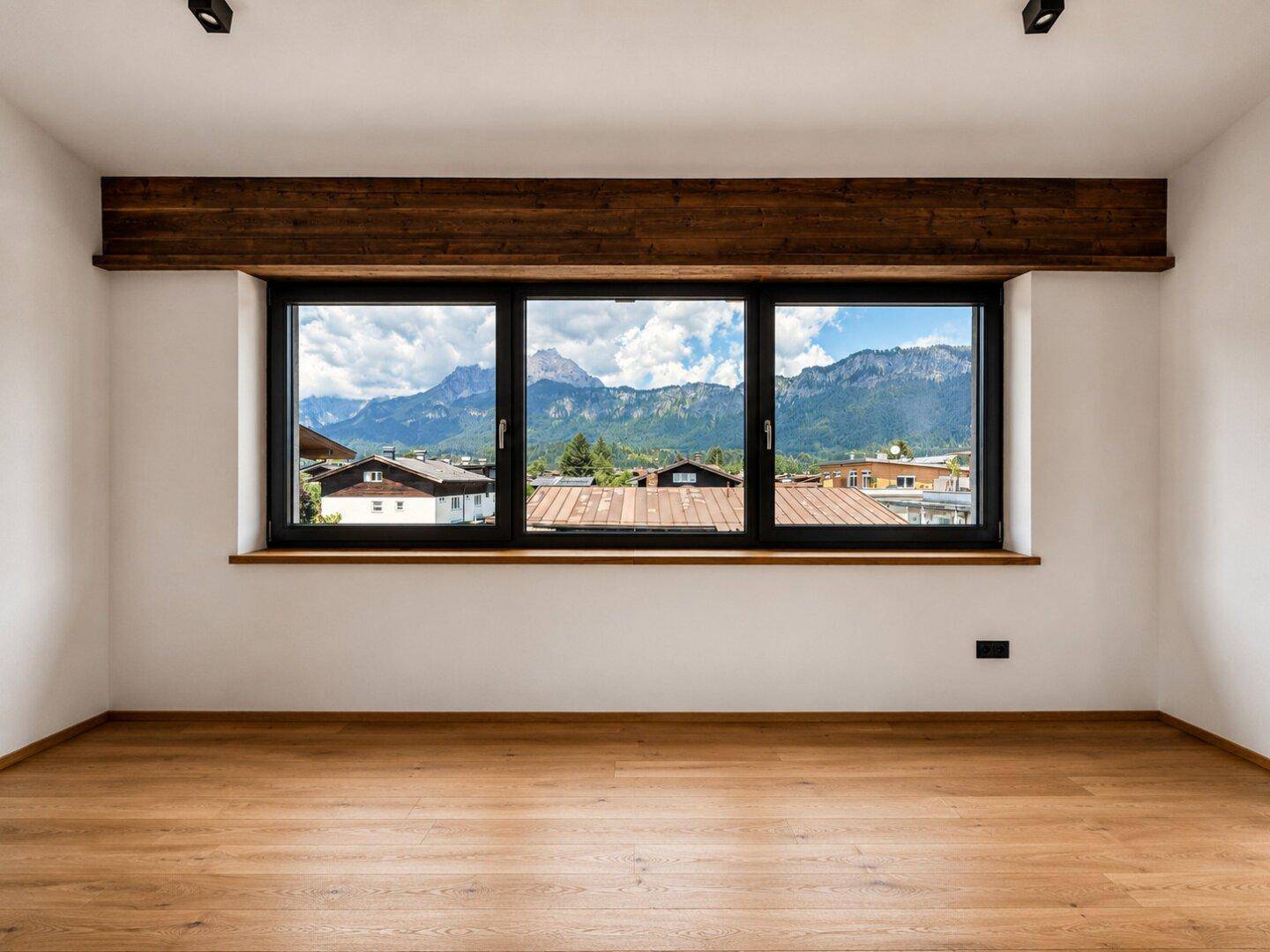 Heller Raum mit Holzbalken und breitem Fenster mit weitem Bergblick.