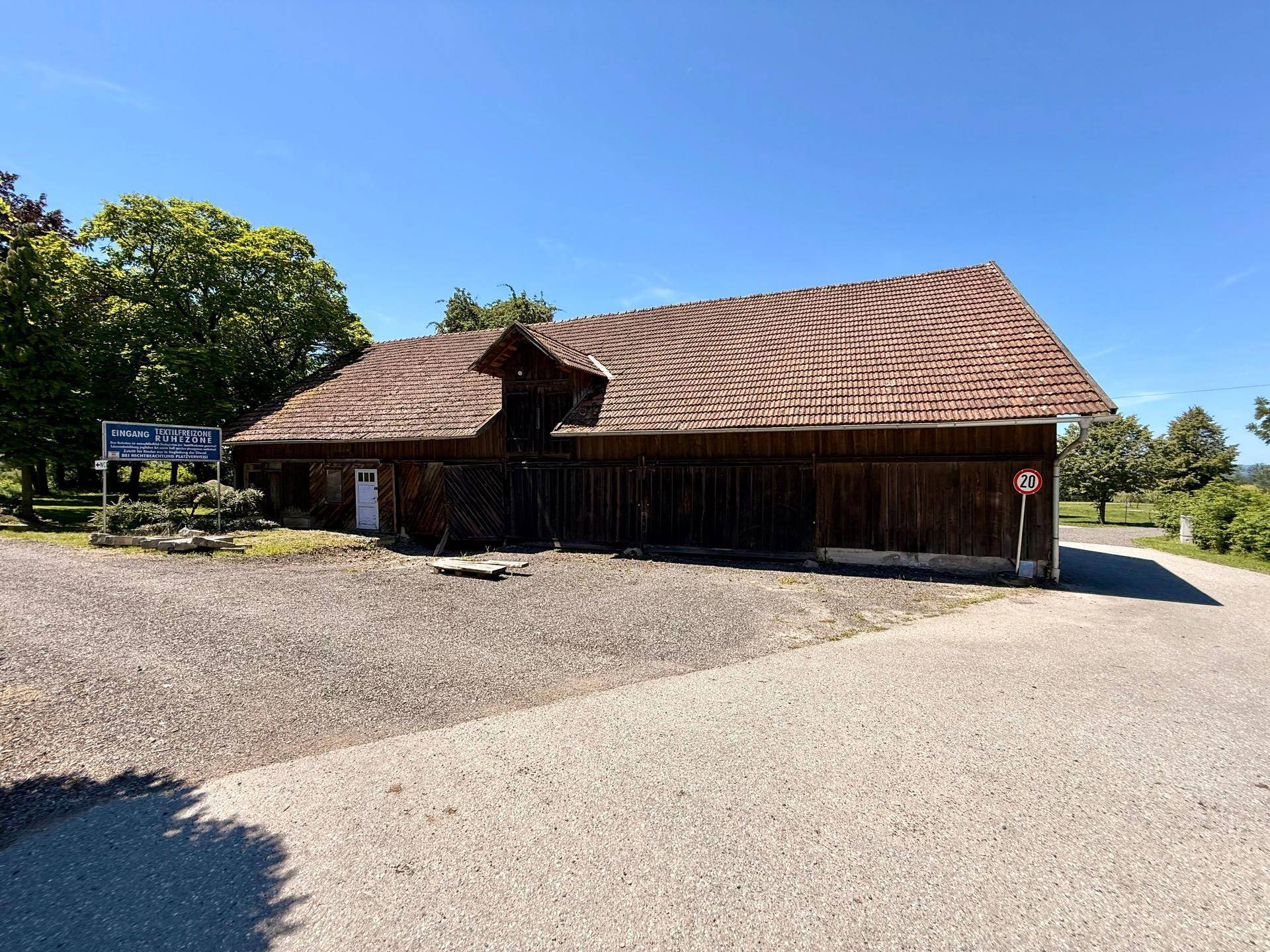 Langes, traditionelles Holzgebäude mit Ziegeldach und einem Kiesvorplatz unter strahlend blauem Himmel.